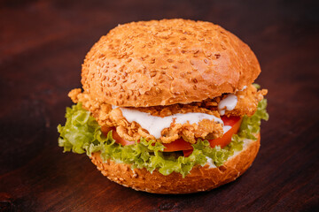Chicken  burger with lettuce, tomatoes, slice of cheese,  and sauce on dark wooden background, close up