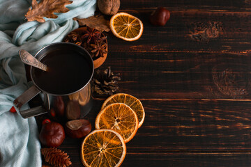 Fototapeta na wymiar Iron mug with black coffee, spices, dry oranges, on a background of a scarf, dry leaves on a wooden table. Autumn mood, a warming drink. Copy space.