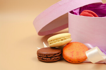 Four brightly colored French Macarons with pink cardboard box on peach background. Free space.