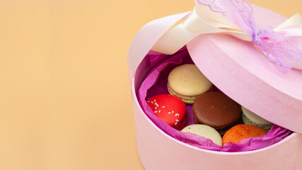 Four brightly colored French Macarons in pink cardboard box on peach background. Free space.
