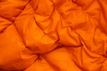 orange fabric of a warm puffed jacket as a background close-up