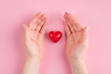 Top above overhead pov first person view photo of female hands around a red heart isolated on pink pastel background with copyspace