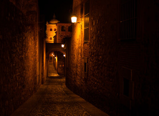 Noche oscura en una calle del casco histórico de Cáceres alumbrada levemente con farolas.