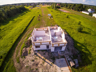 Aerial view on detached house under construction. House in basic state. Located on green plot in small village. Lack of wooden roof structure. Meadows 