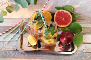 Detox cocktail of organic fruits, berries and mint leaves in glass cups on a wooden table, home kitchen, healthy lifestyle