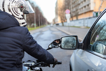 Motorcyclist stands by side with a car on the road, lateral rear mirrors are close to each other,...