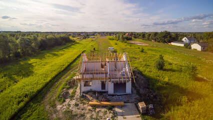 Aerial view on detached house under construction. House Ii basic state. Located on green plot in small village. Wooden roof structure. Meadows around.
