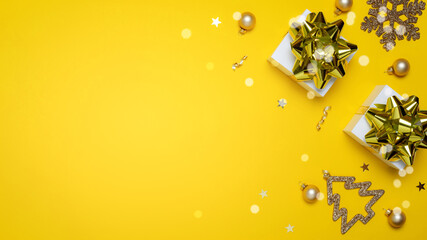 Happy xmas. White gift box with golden color ribbon, New Year balls and sparkling lights in Christmas composition on dark yellow background for greeting card. Copy space. Winter holidays, New Year.