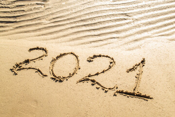 Drawing on wavy sand texture. Inscription 2021 on sea or ocean shore. Top view, copy space. New year and Christmas concept.