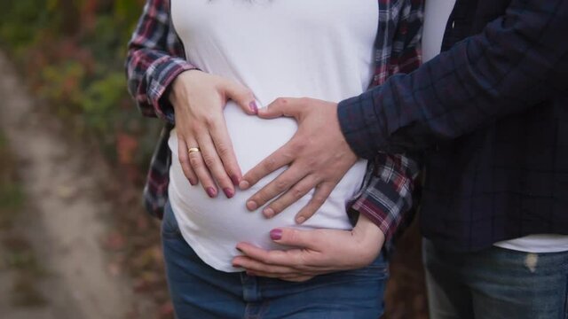 Young couple of future mom and dad depict a heart sign with their hands on the belly of a pregnant girl. 