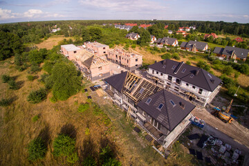 Aerial view on detached houses under construction. House in basic state. Located on green plot in small village. Wooden roof structure. Meadows around.