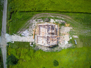 Top-down view on detached house under construction. House In basic state. Located on green plot in small village. Wooden roof structure. Meadows around.