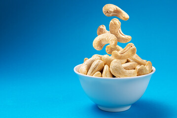 Falling cashew nuts into bowl on blue background