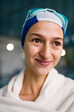 Girl swimmer or swimming coach stands in a swimming cap and goggles, covered with a towel. Happy woman sportswoman