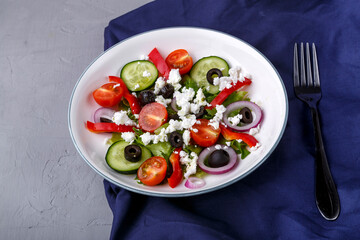 Light plate of Greek salad on a blue napkin on a concrete background.