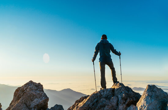 Young hiker Man standing with trekking poles on a cliff edge and looking at Tatra mountains valley covered with clouds. Successful Velky Rozsutec 1610m summit concept image.