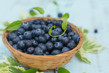 Heap of fresh blueberries and leaves in a basket on white wooden background. Healthy eating and diet food concept.