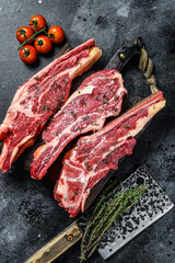 Assortment of raw cuts beef meat steaks on the bone. Black background. Top view