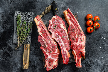 Assortment of raw cuts beef meat steaks on the bone. Black background. Top view