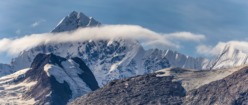 Beautiful panoramic view of a mountain peak covered with ice and snow, surrounded with fluffy couds in Alaska. Blue sky as a background