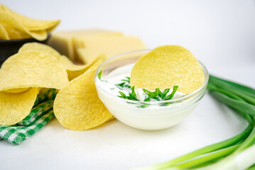 Take a chips from a bowl and dip it in a sour cream sauce with green onion.