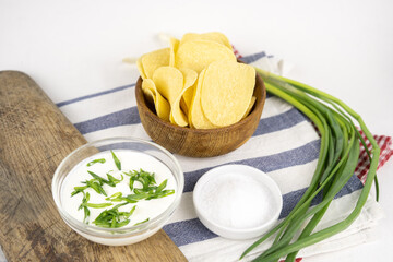 Chips in a wooden bowl with sour cream and green onion.