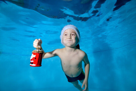 A cheerful little boy swims underwater in a pool with puffy cheeks and holds a Christmas toy in his hand. Portrait. Close up. Horizontal orientation of the image