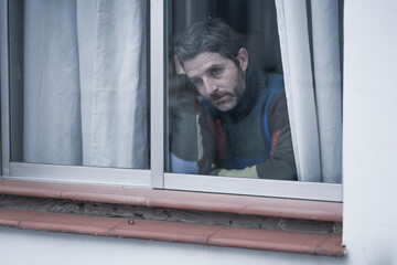 dramatic portrait of attractive sad and depressed mid adult man looking through home window feeling worried and desperate suffering depression problem thoughtful in pain