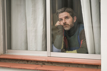 dramatic portrait of attractive sad and depressed mid adult man looking through home window feeling worried and desperate suffering depression problem thoughtful in pain