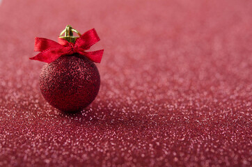 Red Christmas ball with a bow on a red surface.