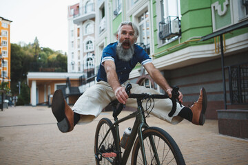 Senior bearded man looking funny, riding bicycle, screaming lifting his legs in the air