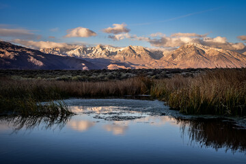 Naklejka na ściany i meble First morning light illuminates mountains with darker valley wetlands grasses reflection in water