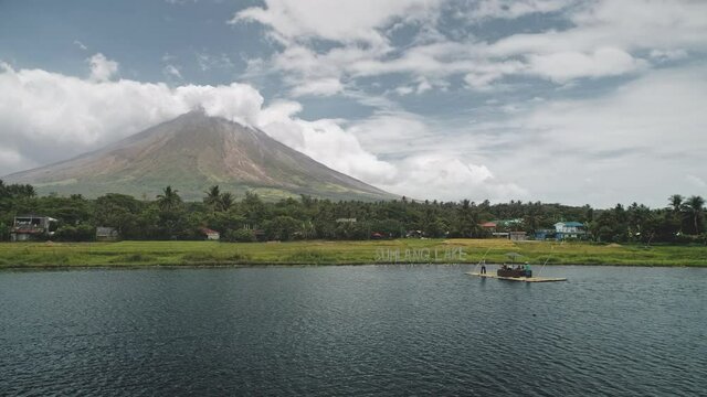 Tropic volcano at lake coast aerial. Tourist cruise at boat at green grass valley at shore. Countryside cottages at palm trees. Nobody nature landscape of Philippines mount Mayon at Legazpi town