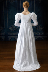 A Regency woman wearing a white muslin dress standing alone in a room