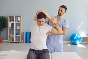 Chiropractor or physiotherapist examining young man's arm to help him cure health problems
