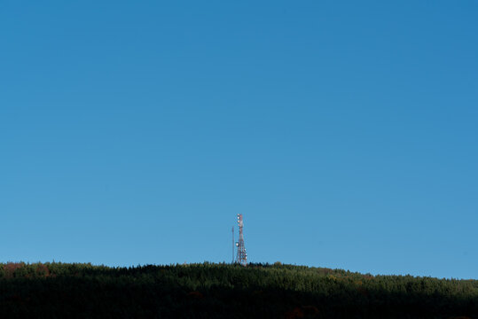 A telecommunications tower on top of forest hill with clear blue sky lots of copy space for advert text clean sharp colors and focus