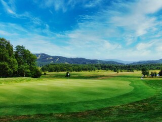 Obraz premium Golf course green the with beautiful blue sky and white clouds in the background.
