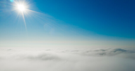 Sun rays shining in the blue sky above white and fluffy clouds