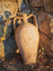 old greek amphora in cone of stone wall in sun lights