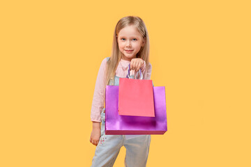 Fototapeta premium A cute girl looks at the camera and holds shopping bags in her hands. Gifts for the holidays. Yellow isolated background.
