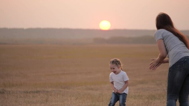 mom and happy baby throw disc, cheerful baby jumps and rejoices. happy family mom and child are playing on field with flying disc at sunset. mother and little healthy daughter have fun together.