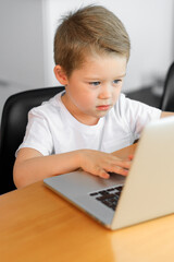 A young boy using a laptop computer sitting on top of a tableundefined at home