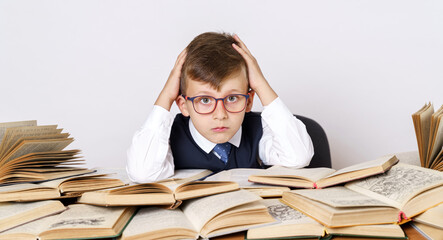 Education concept. The student does his homework, holds his head with his hands and looks at the camera. There are many open books on the table.