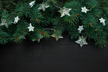 Christmas tree branches with New Year's decor and stars on a dark wooden background.