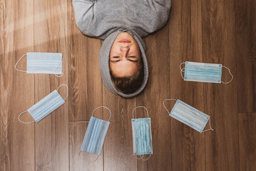 the guy is lying on the floor, a halo of medical masks around his head Sad teenage boy confined at...