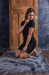 Beautiful young woman in black dress sitting on fur skin in front of vintage door