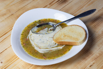 Vegetable cream soup with sour cream, toast, spoon in white plate on wooden background