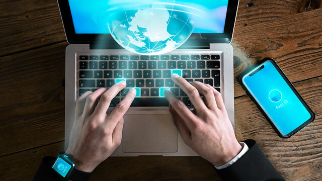 Businessman in home office communicates with colleagues via laptop, smartphone and smart watch all over the world - login with face id. Texting and networking.