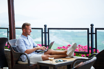 Successful male businessman working on vacation behind a laptop with a mountain view. Online manager workflow. Work outdoors with a beautiful view from the balcony