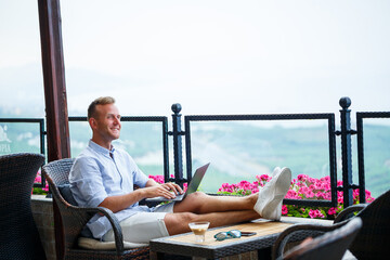 Successful male businessman working on vacation behind a laptop with a mountain view. Online...